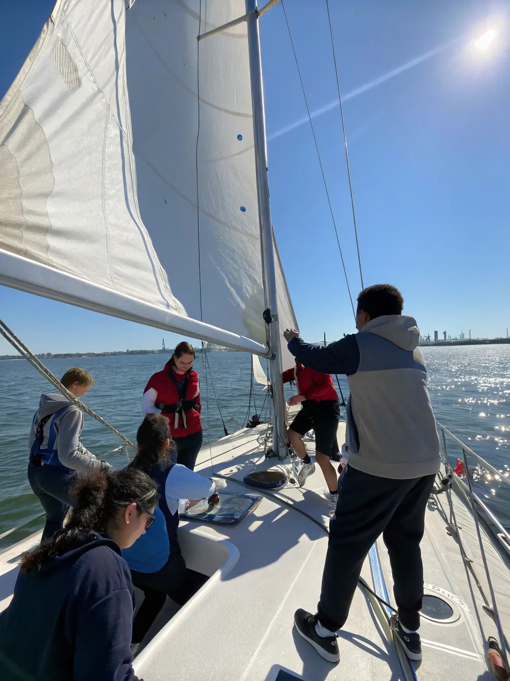 A group of people participating in a sailing workshop, learning about boat handling and navigation techniques, with the Bonne Anse bay in the background.